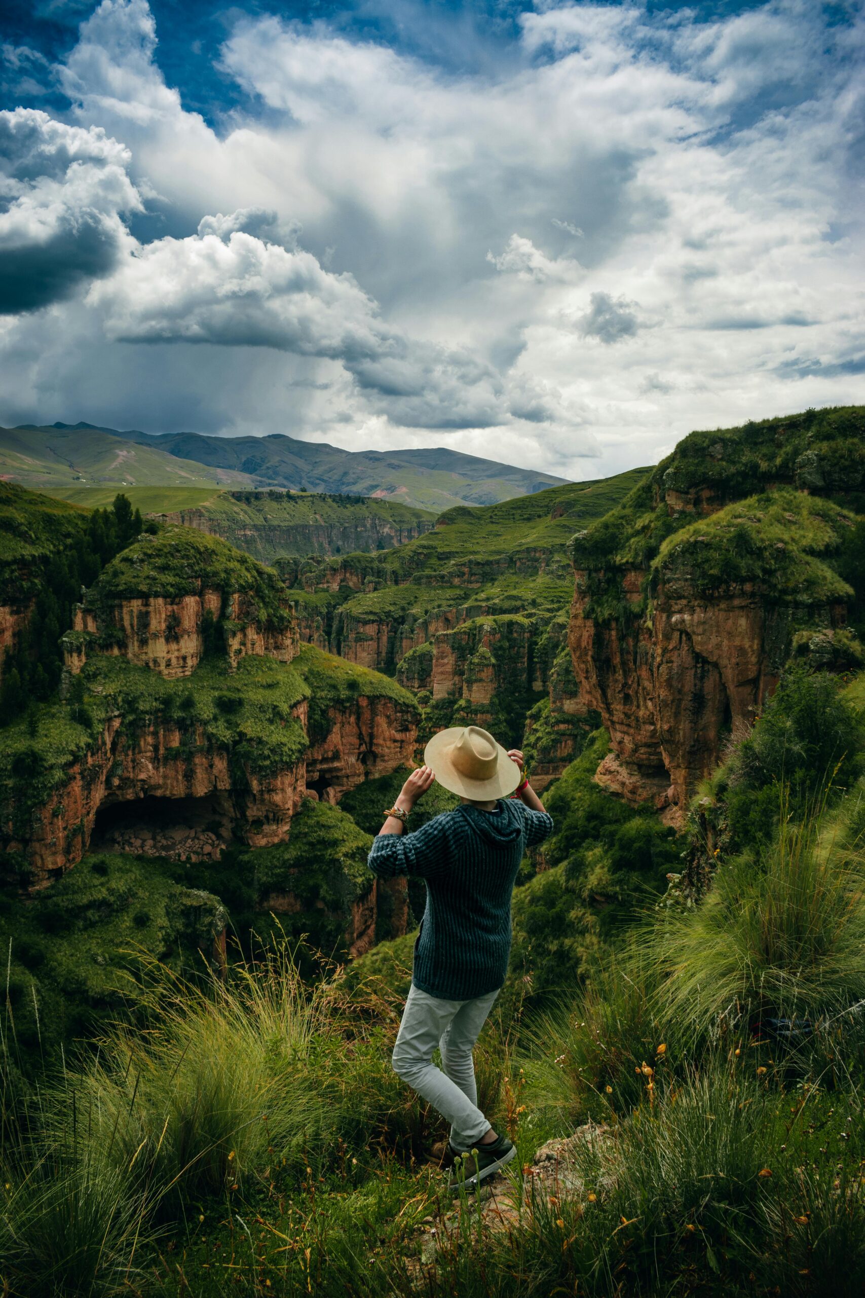 Person with hat overlooking vibrant Cuzco canyon, capturing adventure and natural beauty.