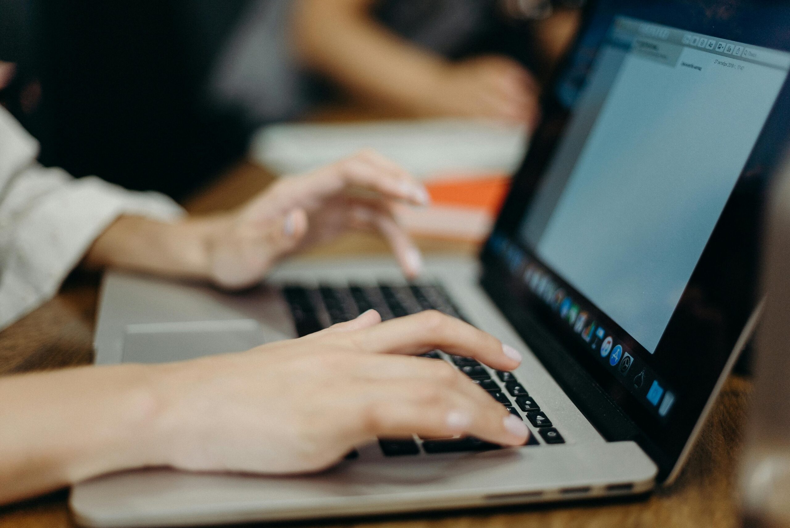 Person typing on a laptop in an office setting. Focus on hands and keyboard.