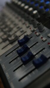 Detailed view of a sound mixer control panel with blue faders and control buttons in a studio setting.